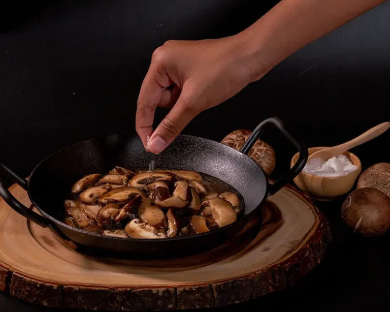 How chefs use finishing salt on hot mushrooms, adjusting salt by hand to control surface texture and flavour.