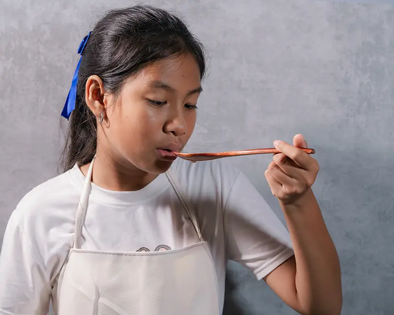 Cook tasting food from a spoon to adjust seasoning, showing how chefs use finishing salt.