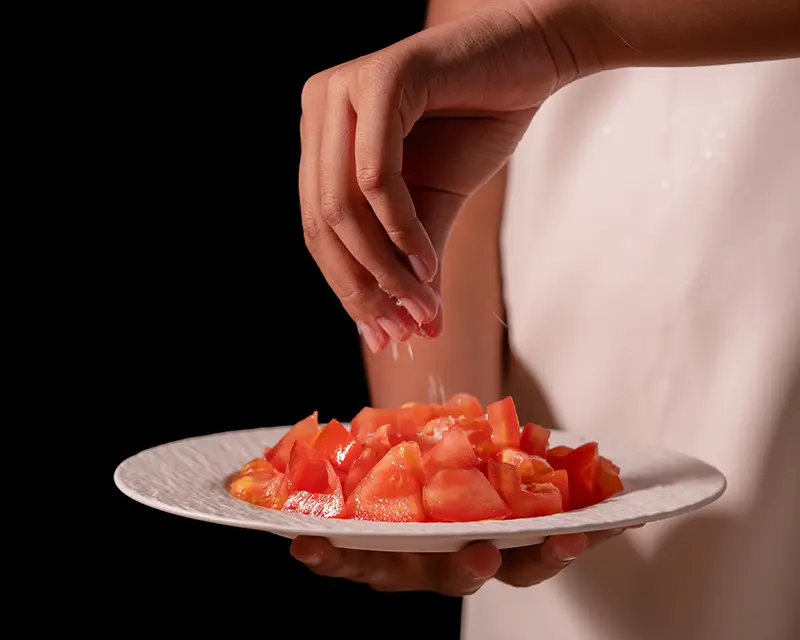 Hand salting chopped tomatoes, showing how to salt tomatoes by taste