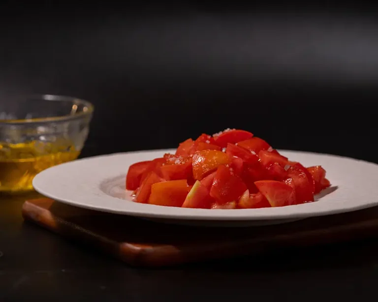 How to salt tomatoes with olive oil, showing chopped tomatoes with finishing salt and olive oil beside the plate
