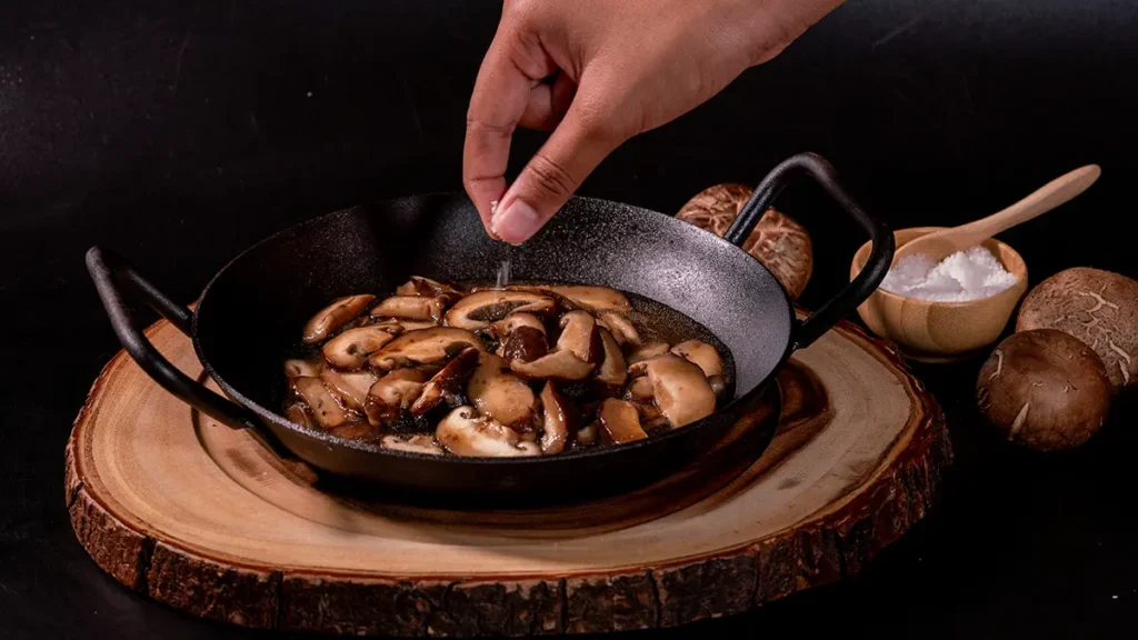 Mushrooms being salted in a pan for a guide on how to salt vegetables for better browning.