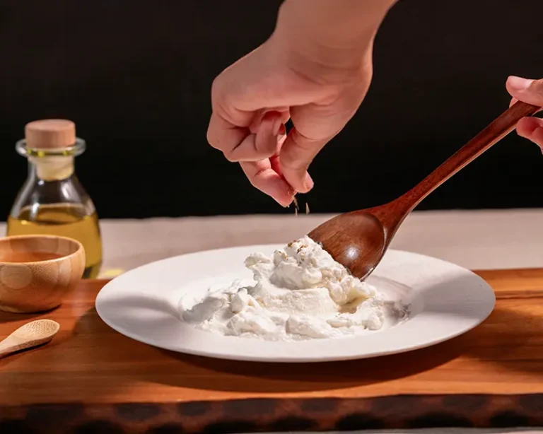 Hand adding salt to yogurt with a spoon, showing how to salt yogurt at the final surface seasoning stage.