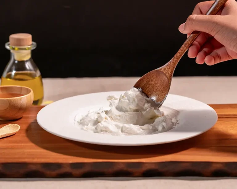 Wooden spoon moving through thick yogurt or labneh, showing how to salt yogurt when the texture holds finishing salt.