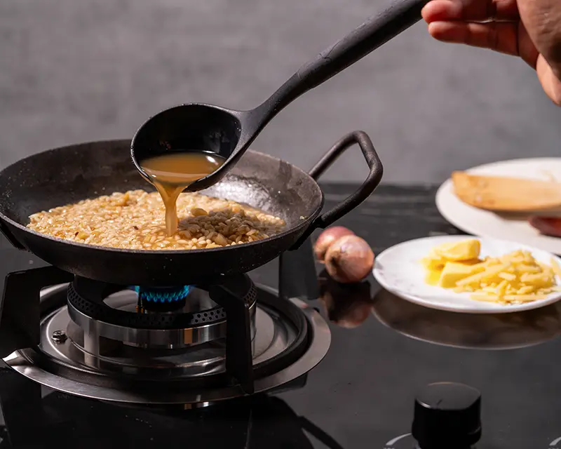 Adding warm stock to risotto while learning how to season risotto for deeper flavour