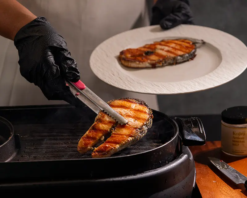 How to season salmon after grilling, shown as a browned salmon steak is lifted from the grill before the final seasoning.