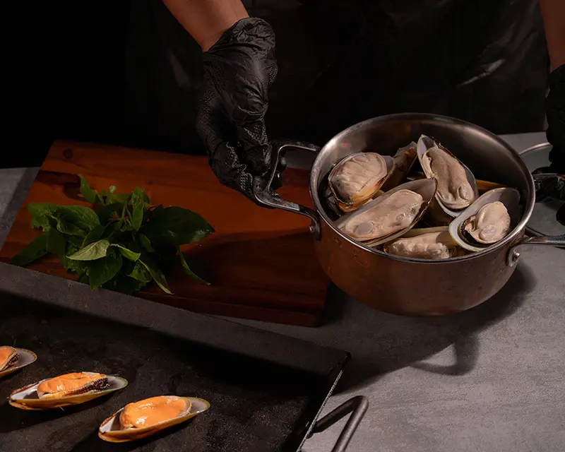 Half-shell mussels arranged in a copper pot for a mussels recipe with preserved lemon, garlic and fresh basil.