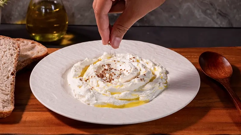 Preserved lemon salt being added to thick yoghurt with olive oil and bread.