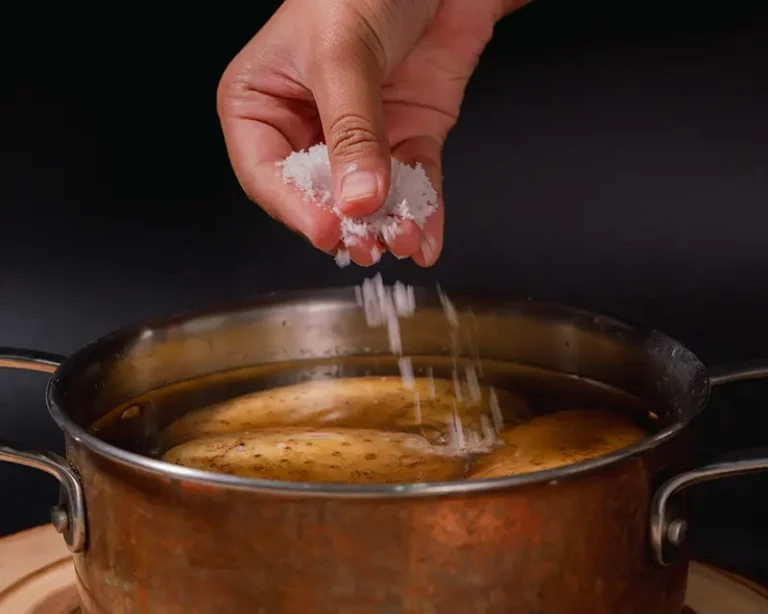 Salt being added to water with whole potatoes in a pot