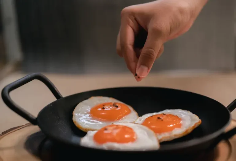Hand sprinkling salt over fried eggs in a pan