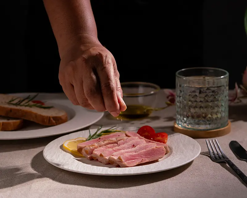 A final pinch of tuna steak seasoning sprinkled over sliced, seared tuna with a pink centre, served with lemon and rosemary.