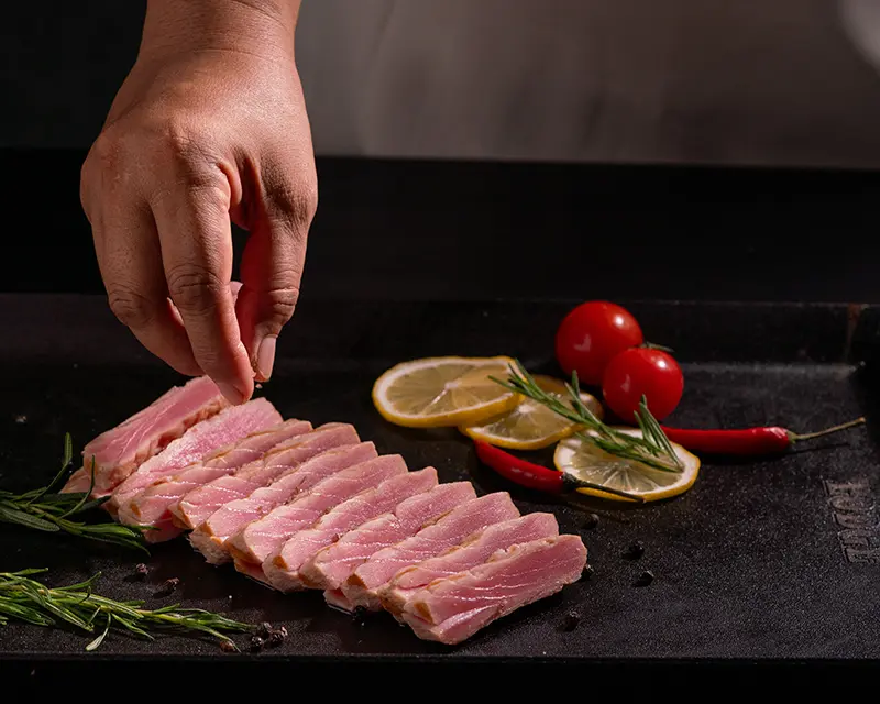 Chef adding a final pinch of salt to sliced tuna steak with a pink centre, demonstrating tuna steak seasoning after searing.