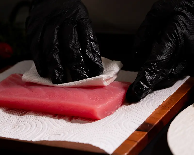 Chef patting a raw tuna steak dry with paper towels before applying tuna steak seasoning and searing.