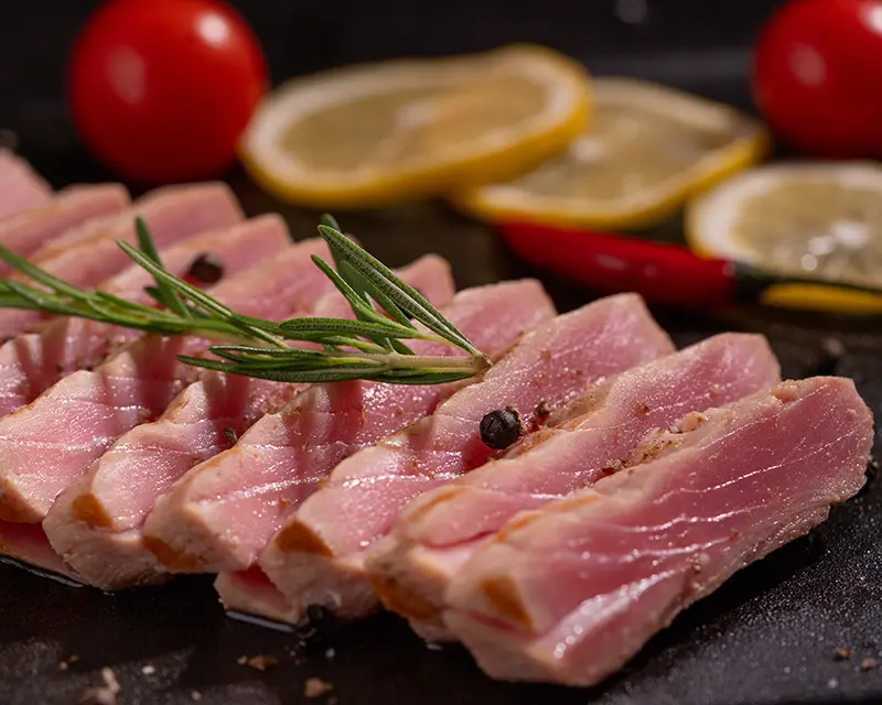 Close-up of sliced tuna steak with a pink centre, lightly seasoned with salt and pepper and served with rosemary and lemon.