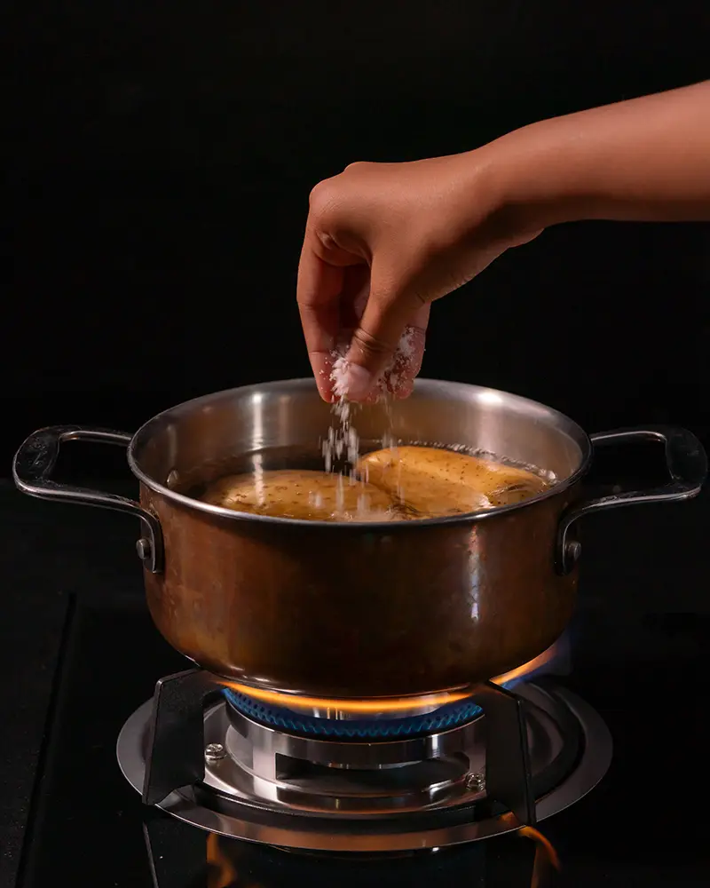 Salt being added to potatoes in boiling water for a guide on when to salt potatoes.
