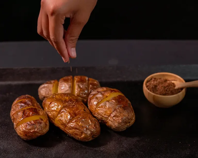 Salt being added to hot roast potatoes, showing when to salt roast potatoes so the crystals grip the crisp edges.