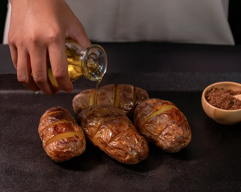 Olive oil being poured over roast potatoes before finishing with salt, showing how hot fat helps when to salt roast potatoes.