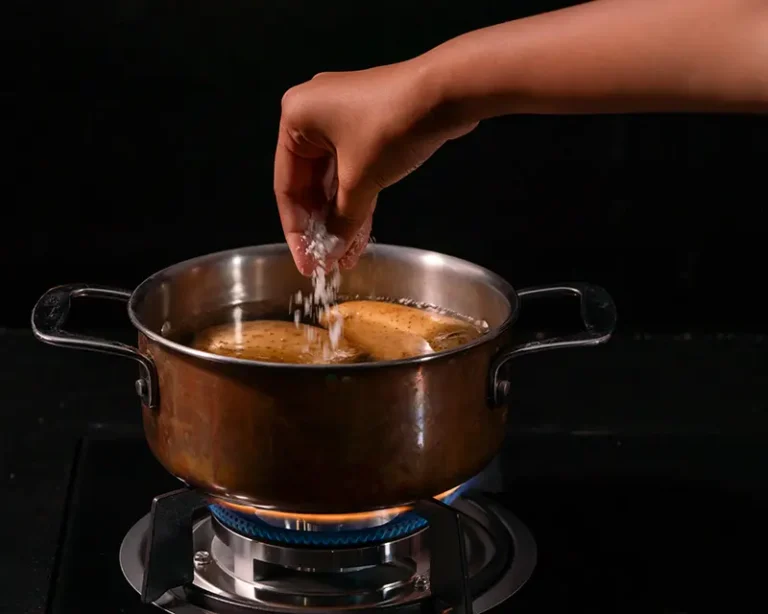 Salt being added to parboiling potatoes, showing when to salt roast potatoes so the centre is seasoned before roasting.
