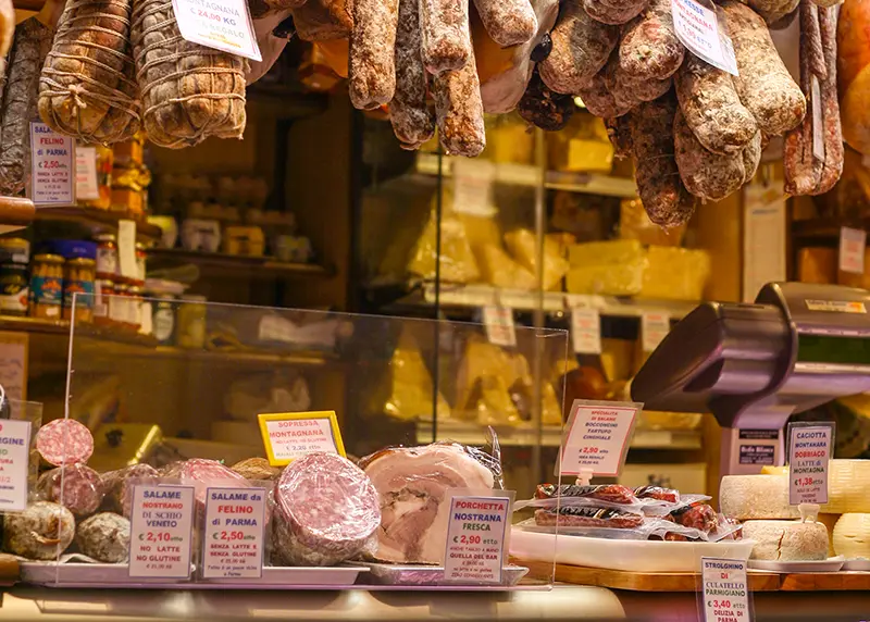 Traditional Italian delicatessen with hanging cured meats and a well-stocked speciality food counter, illustrating wholesale gourmet food opportunities for Maison Kojira.