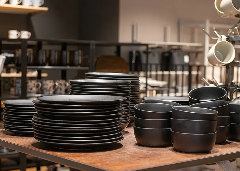 Stacks of matte black plates and bowls displayed in a specialist tableware shop, illustrating how wholesale gourmet food from Maison Kojira complements beautiful cookware and tableware.
