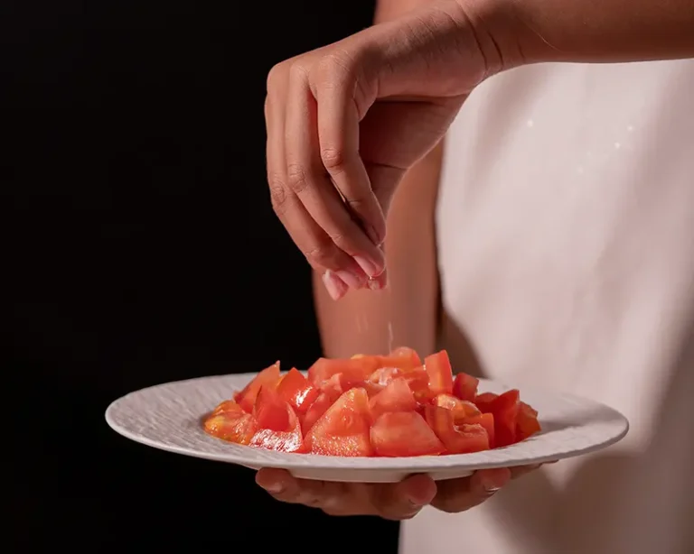 Salt being added to tomatoes, showing why salt makes food taste better by changing how ingredients are perceived.